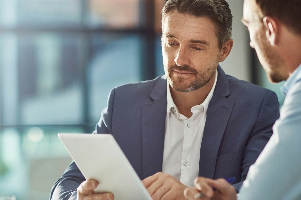 Entrepreneur français dans un espace de coworking moderne, consultant des documents d'immatriculation et une tablette affichant le site du Guichet Unique INPI, posture de réflexion concentrée
