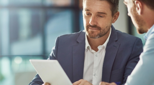 Entrepreneur français dans un espace de coworking moderne, consultant des documents d'immatriculation et une tablette affichant le site du Guichet Unique INPI, posture de réflexion concentrée